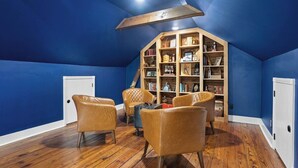 A room with blue walls, wooden flooring, a bookshelf, leather chairs, and a white door. - OC House 914 Crossland Ave (Clarksville)