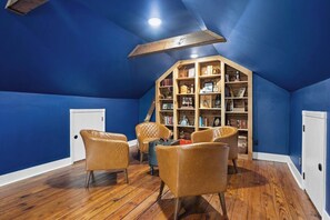 A room with blue walls, wooden flooring, a bookshelf, leather chairs, and a white door. - OC House 914 Crossland Ave (Clarksville)