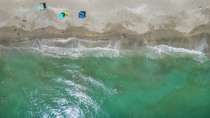 Eine Luftaufnahme eines Strandes mit klarem türkisblauem Wasser, einem sandigen Ufer und mehreren bunten Sonnenschirmen.