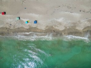 Eine Luftaufnahme eines Strandes mit klarem türkisblauem Wasser, einem sandigen Ufer und mehreren bunten Sonnenschirmen.