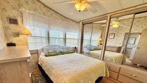 A bedroom with a large bed, a dresser, a mirror, and a window with blinds. - Cal's Retreat N617 (Jensen Beach)