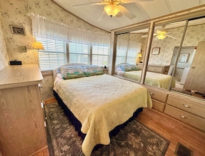 Ein Schlafzimmer mit einem großen Bett, einem Schminktisch, einem Spiegel und einem Fenster mit Jalousien.