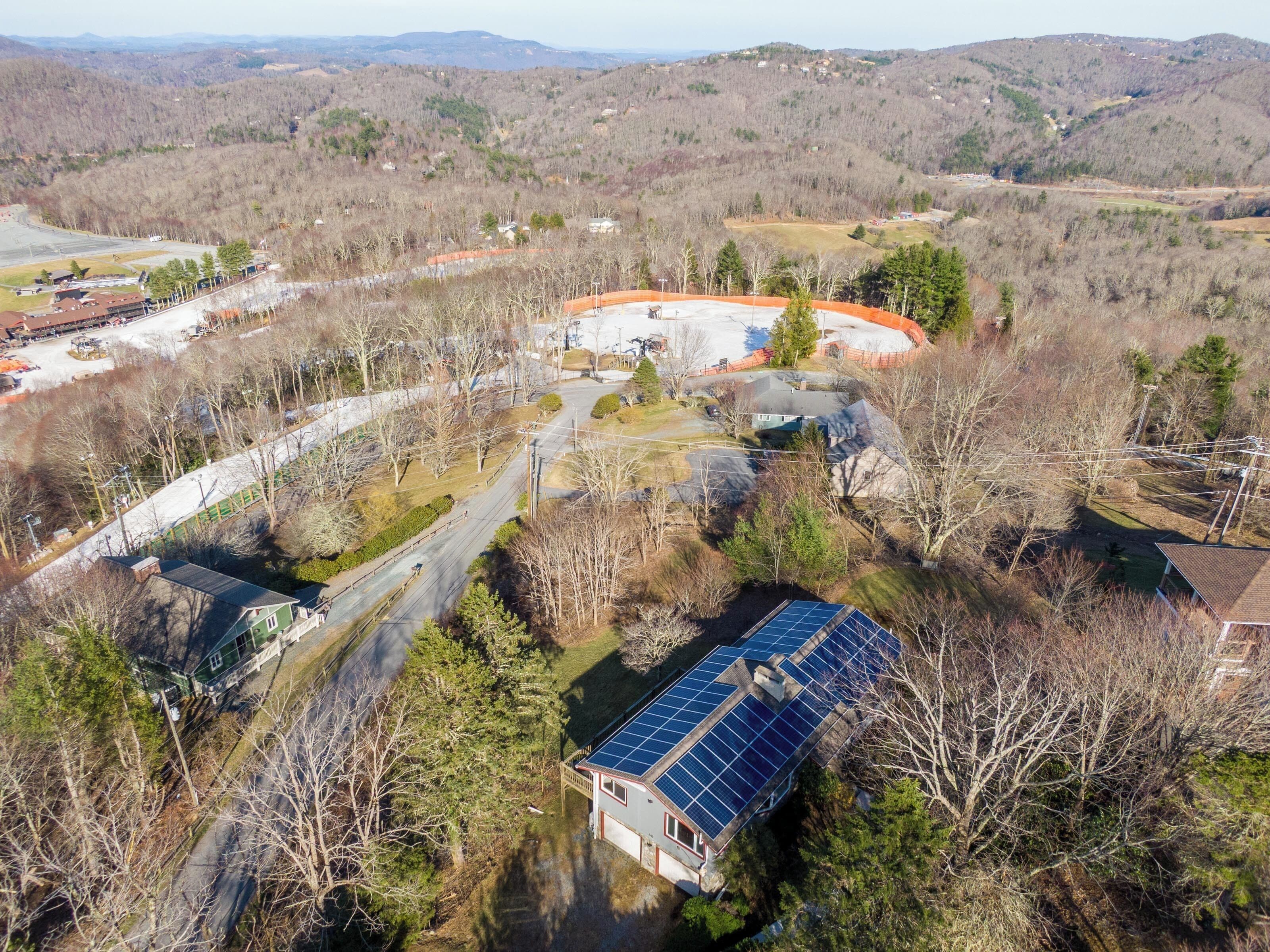 A residential area with a house featuring a solar panel roof, surrounded by trees and a winding road.