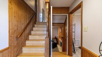 Una escalera de madera conduce a un segundo piso con chimenea y una abertura.