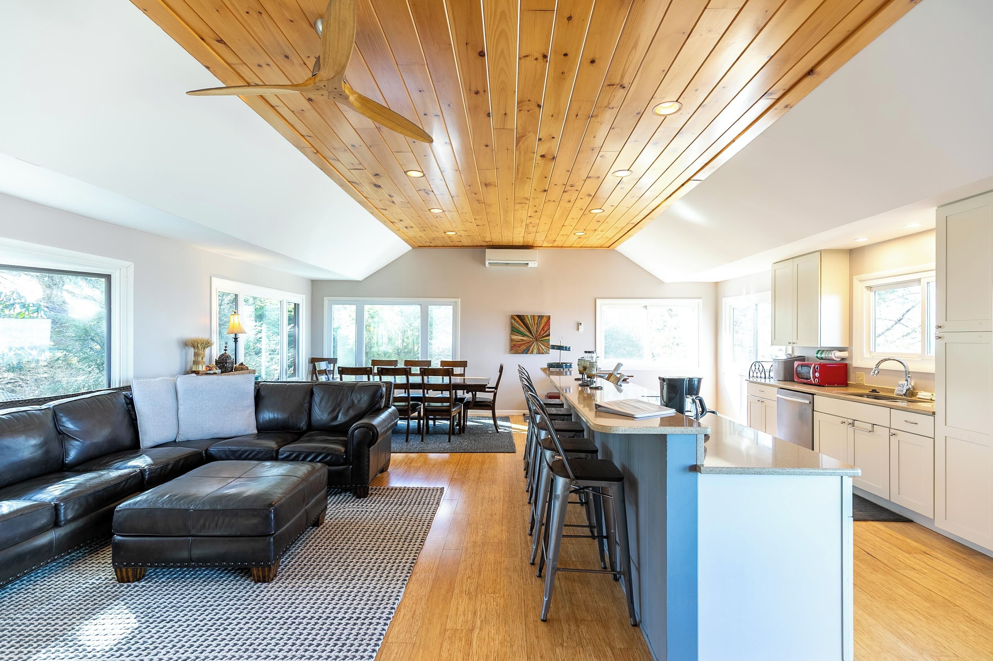 Una cocina moderna con una isla central, techo de madera y ventanas amplias.