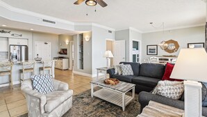 A spacious living room with a gray sofa, a coffee table, and a dining area with a kitchen in the background. - Gulf Crest 2005 (Panama City Beach)