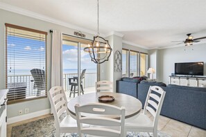 Ein Essbereich mit rundem Tisch und weißen Stühlen, ein Balkon mit Aussicht, ein Wohnzimmer mit Sofa und Fernseher sowie ein Deckenventilator.