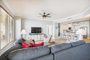 Ein geräumiges Wohnzimmer mit grauem Sofa, einem Flachbildfernseher und einem Deckenventilator.