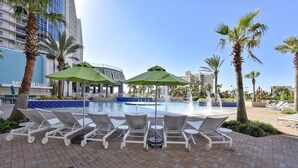 A poolside area with lounge chairs and umbrellas, a fountain, and a building with a blue facade in the background. - Laketown Wharf 835 (Panama City Beach)