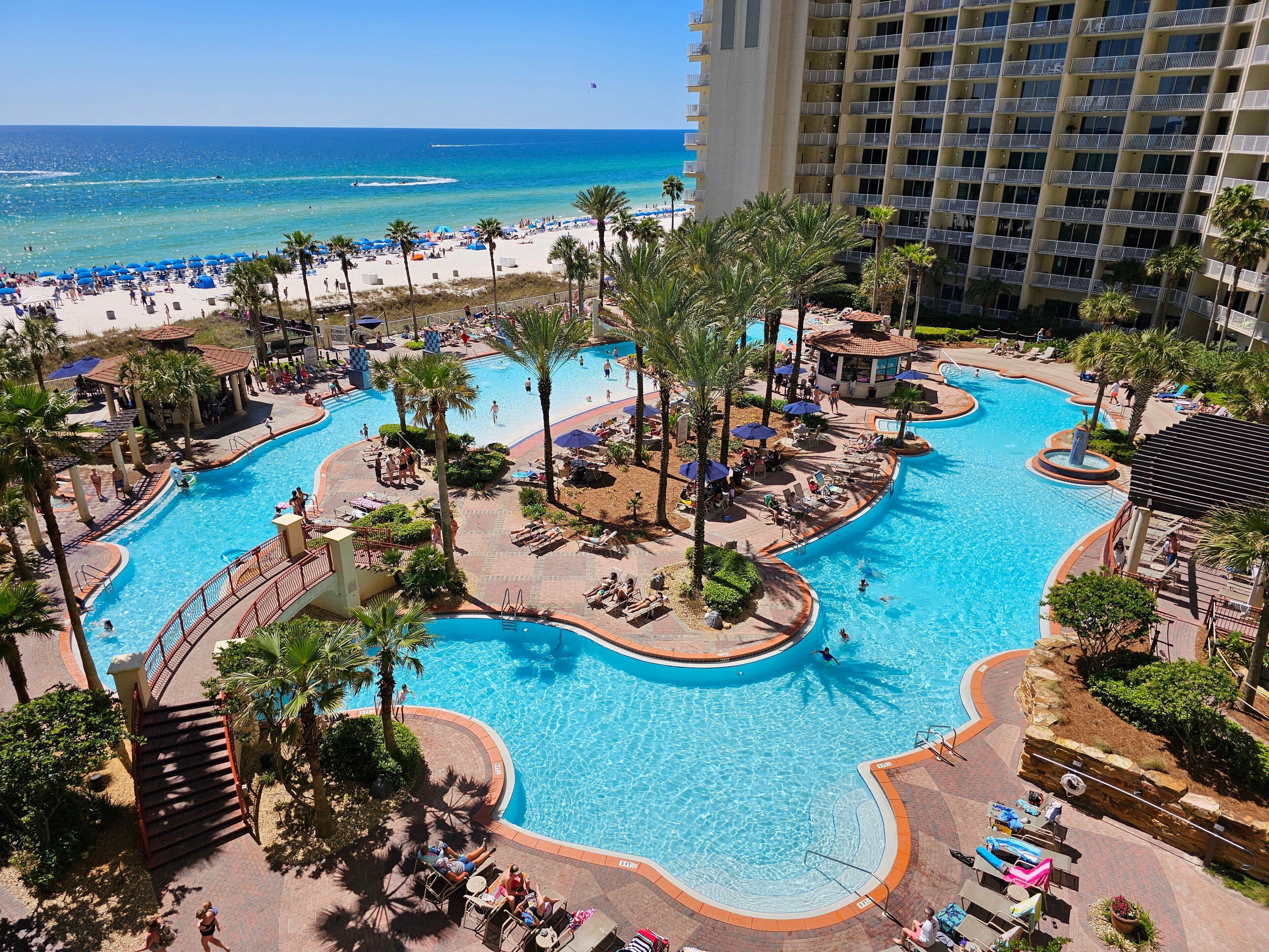 Ein Resort mit großem Poolbereich, einem Strand und einem Hochhaus.