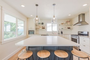 A modern kitchen with a large island, pendant lights, and a view to the outside.