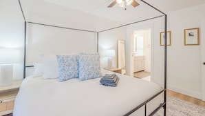 A modern bedroom with a four-poster bed, a ceiling fan, and a view into the bathroom. - 72 S Orem Upstairs Only (Orem)