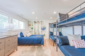 A bedroom with a bunk bed, a single bed, a dresser, and a window with blinds.