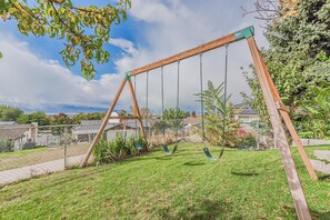 A wooden swing set in a grassy backyard with a view of houses in the background.