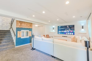 A modern living room with a staircase, a white sofa, and a flat-screen TV displaying a sports channel.