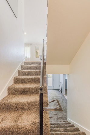 A carpeted staircase with a handrail, white walls, and a framed picture on the wall.