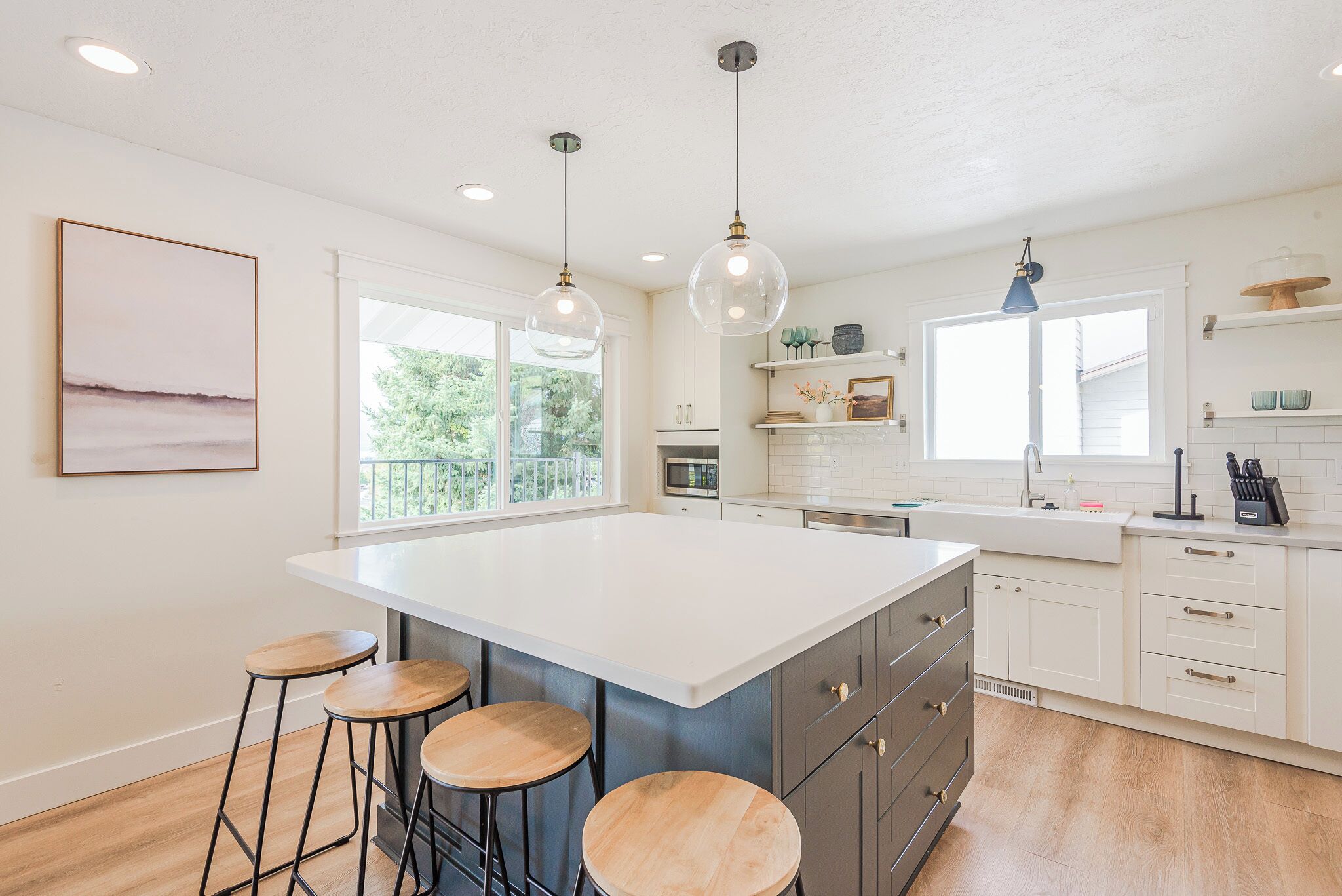 A kitchen with a large island, bar stools, pendant lighting, and a view of the outdoors.