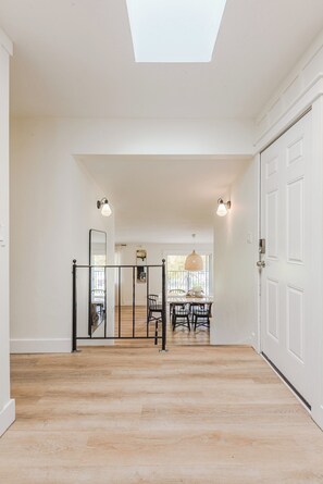A spacious hallway with a skylight, a dining area with a table and chairs, and a white door on the right.