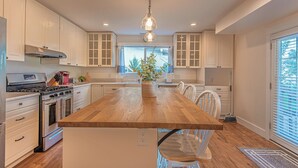 A kitchen with white cabinets, a wooden island, stainless steel appliances, and a hanging light fixture.