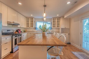 A kitchen with white cabinets, a wooden island, stainless steel appliances, and a hanging light fixture.