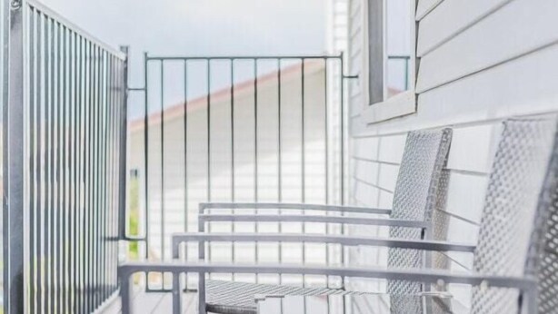 A balcony with metal chairs and a table, white siding on the building, and a metal railing.