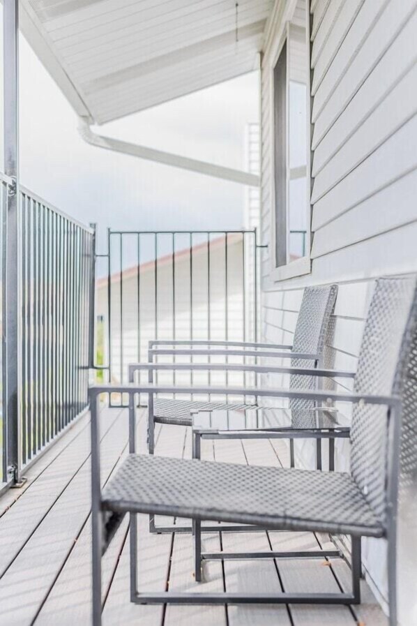 A balcony with metal chairs and a table, white siding on the building, and a metal railing.