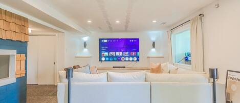 A modern living room with a large flat-screen TV mounted on the wall, a white sofa, and a small coffee table.