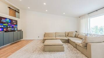 A modern living room with a sectional sofa, a flat-screen TV, and a wooden floor.