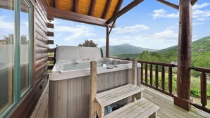 Eine Holzterrasse mit Whirlpool, Holzgeländern und Blick auf grüne Hügel.