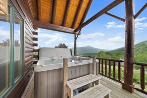 Eine Holzterrasse mit Whirlpool, Holzgeländern und Blick auf grüne Hügel.