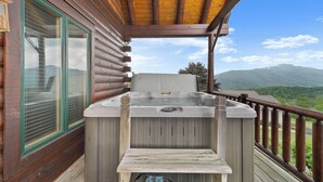 Eine Holzblockhütte mit Whirlpool auf einer Terrasse, mit Blick auf eine gebirgige Landschaft.