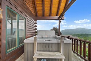 Eine Holzblockhütte mit Whirlpool auf einer Terrasse, mit Blick auf eine gebirgige Landschaft.