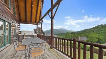 A wooden deck with a table and chairs, overlooking a mountainous landscape.
