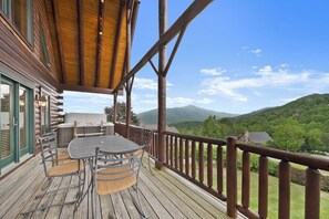 Eine Holzterrasse mit Tisch und Stühlen mit Blick auf eine gebirgige Landschaft.