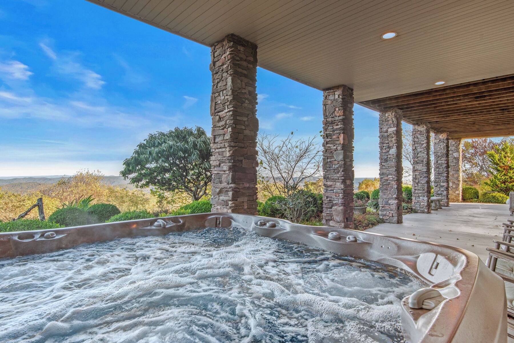 A hot tub with stone pillars, a covered patio, and a view of the landscape.