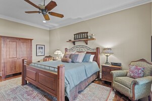 Un dormitorio con cama de madera, mesita de noche, silla, ventilador de techo y estante en la pared.