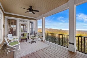 A covered porch with a ceiling fan, a view of a hilly landscape, and outdoor seating with chairs and a table.