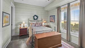 Um quarto com uma cama, duas mesas de cabeceira, um ventilador de teto e uma janela grande com cortinas.