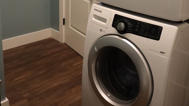 A stacked front-loading Samsung washer and dryer in a laundry room with a wooden floor and a white door. - Rocky Hill Retreat (Rocky Hill)