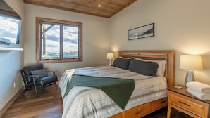 A bedroom with a bed, a chair, a nightstand, a lamp, and a window with a view. - Up and Away at Eagles Nest (Banner Elk)
