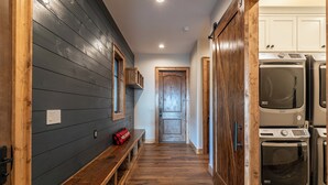 A laundry room with stacked washers and dryers, a wooden bench, and a door leading to another room. - Up and Away at Eagles Nest (Banner Elk)