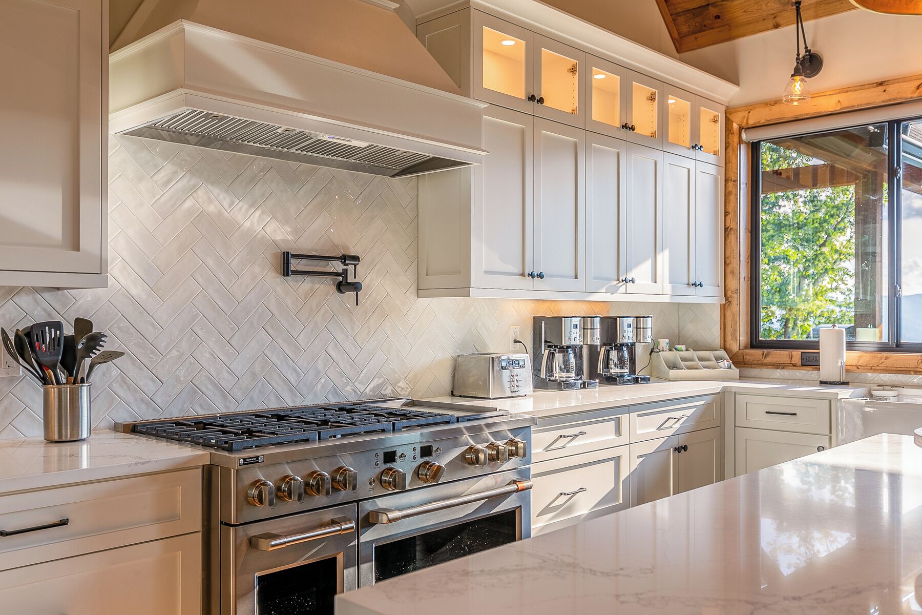 A modern kitchen with white cabinetry, a stainless steel stove, and a large window providing natural light.
