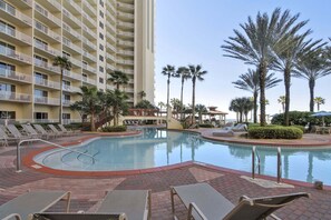 A swimming pool with lounge chairs, palm trees, and a tall building with balconies. - Shores of Panama 1807 (Panama City Beach)