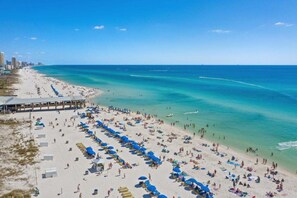A beach with rows of sun loungers and umbrellas, a pier, and a clear blue sea. - Shores of Panama 1807 (Panama City Beach)