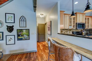 A kitchen with wooden cabinets, a microwave, and a stone backsplash. - Adventure Hideaway at Eagles Nest (Banner Elk)