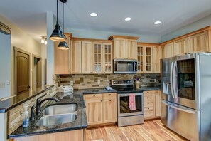 A modern kitchen with wooden cabinets, a stainless steel refrigerator, a microwave, and a double sink. - Adventure Hideaway at Eagles Nest (Banner Elk)