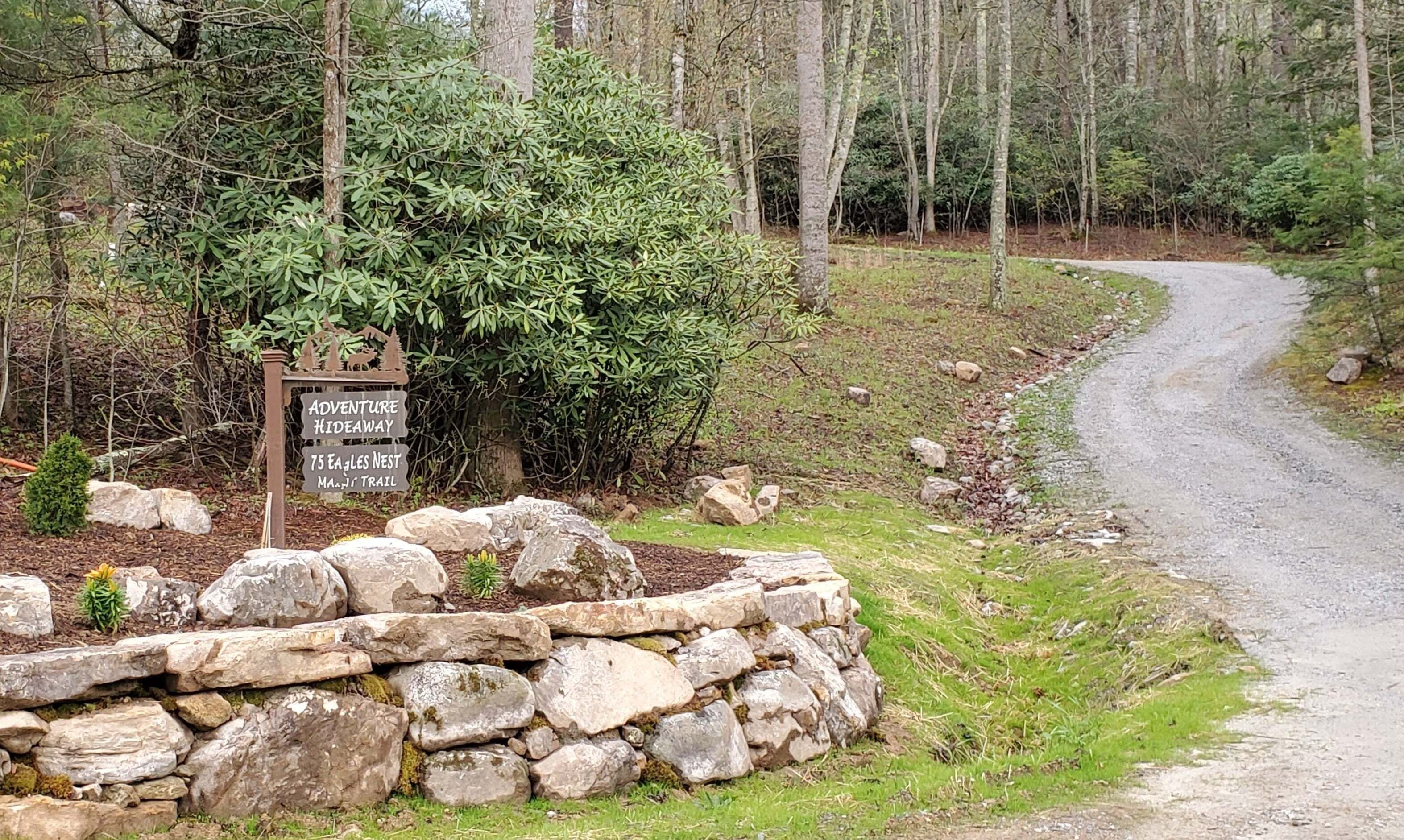 A stone wall with a sign indicating an Adventure Hideaway and 75 Eagles Nest on Mann's Trail.