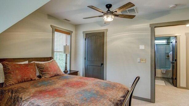 A bedroom with a bed, a ceiling fan, a door, and a bathroom visible through an open door. - Adventure Hideaway at Eagles Nest (Banner Elk)