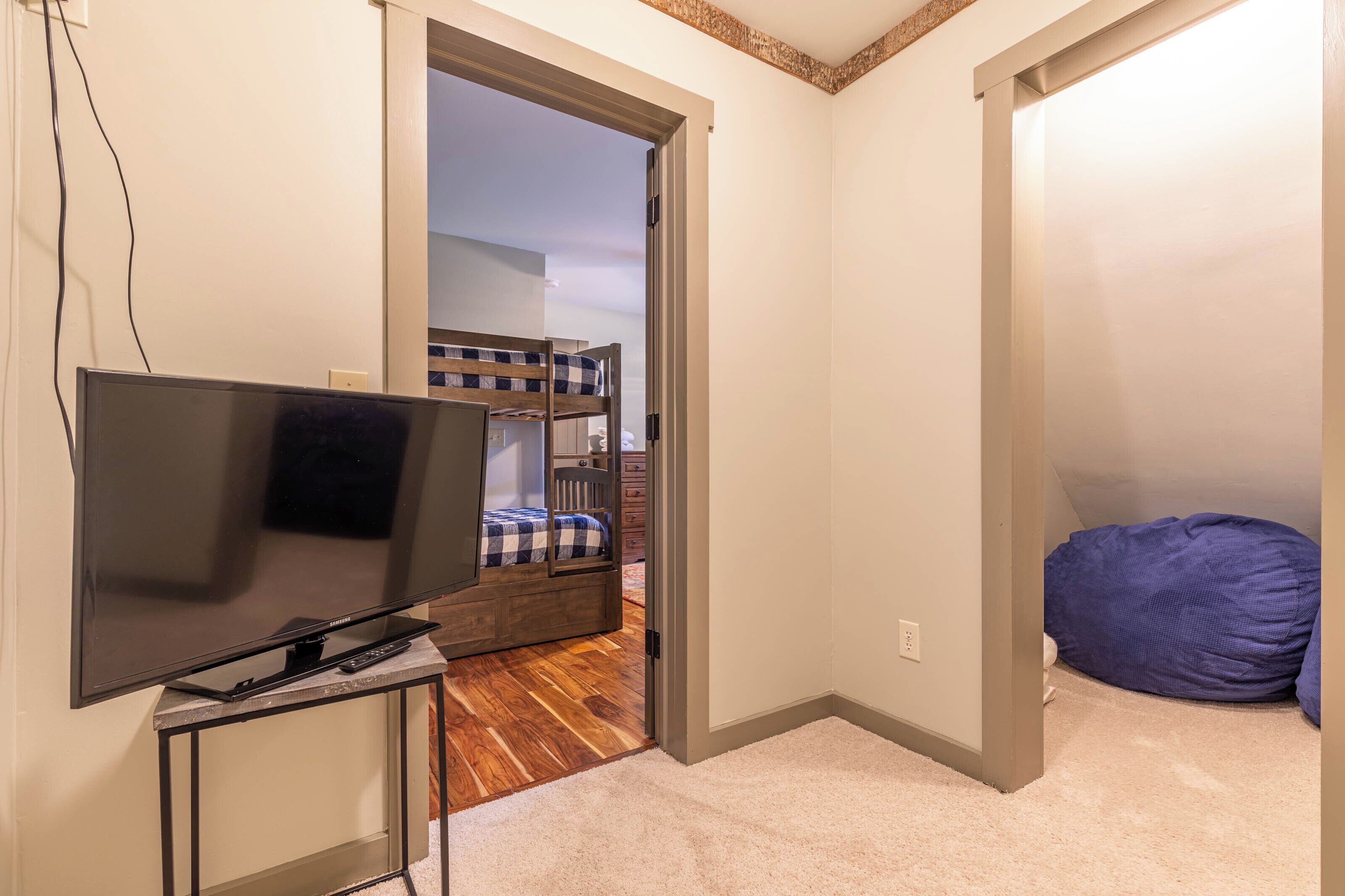 Una stanza con una TV su un mobile, un letto a castello sullo sfondo e una poltrona sacco.