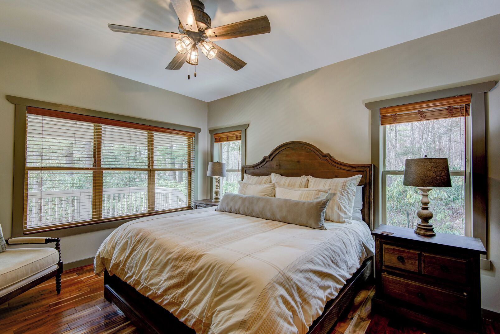 A bedroom with a large bed, a ceiling fan, and a nightstand with a lamp.